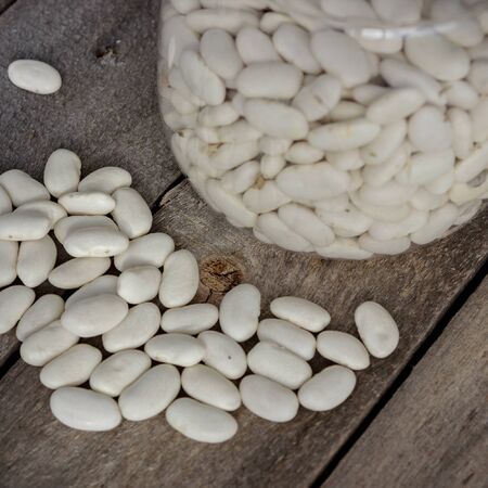 White bean seeds in a jar and scattered on the old table