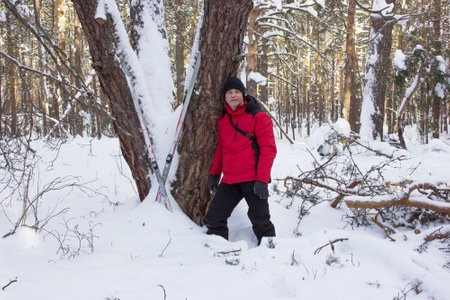 Man walked through a snowy winter forest, tired and leaning against a treeの写真素材