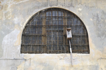 Starling house attached near a window of old prison. The window is taken away by a lattice and tightened by a metal gridの写真素材