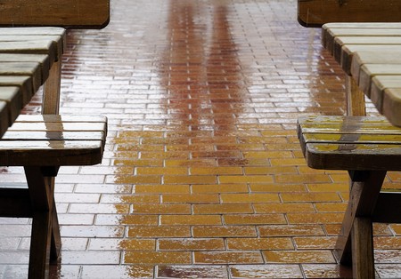 Outdoor cafe on a rainy day. Reflection of people on wet sidewalk, rain drops fall on benchesの写真素材