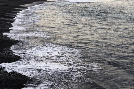 Sea surf rolls on a black beachの写真素材