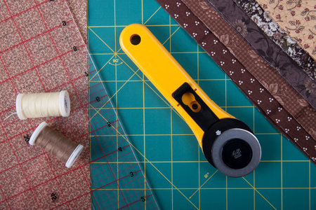 On the mat for patchwork sewing a knife for patchwork, a ruler, a patchwork napkin and threads