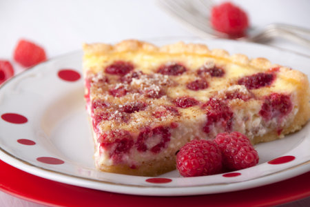 Sand cake with curd filling and raspberries in a red a plate on a white wooden tableの写真素材