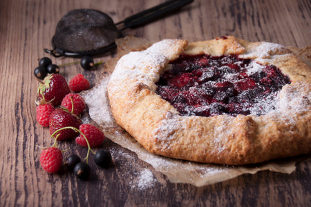 Galette with berries raspberries, strawberries and black currants with sugar powder on a wooden tableの写真素材