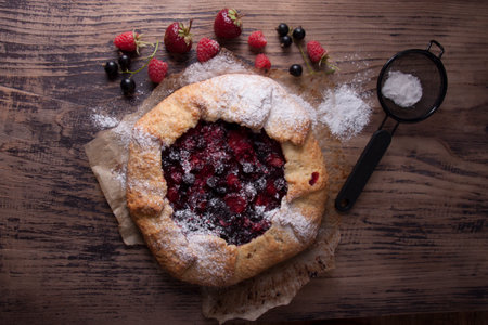 Galette with berries raspberries, strawberries and black currants with sugar powder on a wooden tableの写真素材
