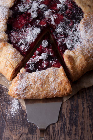 Galette with berries raspberries, strawberries and black currants with sugar powder on a wooden tableの写真素材
