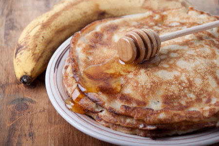 A pile of banana pancakes with honey on a plate a vi banana on an old wooden tableの写真素材