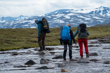 Hiking Friends Manage to wade across the river with helping hand and team work during long Hike in Padjelanta National Park, northern Europe.の写真素材