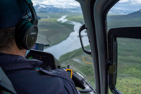 Padjelanta, Sweden - July 2020: Close up of a Helicopter Pilot in Cockpit flying aircraft over Rivers and Forests in Padjelanta and Sarek National Park Northern Sweden, Lapland.のeditorial素材