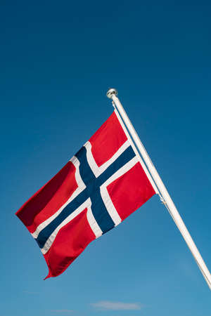 Full National Flag of Norway on Flagpole With Lofoten Background and clear blue sky.の写真素材