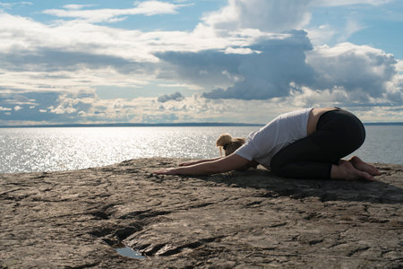 Woman practicing Yoga, meditation or stretching close to water on Cliff doing different poses on beautiful landscape. Concept of finding ideal calm meditation place, finding yourself and Healthy Life.の写真素材