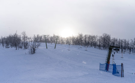 Wintertime Light Snowstorm at the Ski Resort with fresh Powder snowfall illuminated by evening sun in Ski Lift Piste.の写真素材