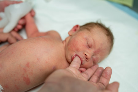A newborn baby lies peacefully on a white blanket with eyes closed, gently sucking on a parents finger. This tender moment captures the bond and comfort between parent and child.の写真素材