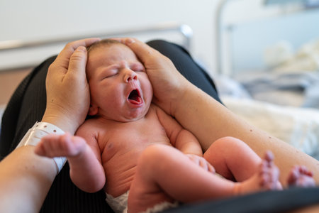 A newborn signaling hunger while being held by a parent in a hospital. The image captures the intimate moment and the importance of responsive feedingの写真素材