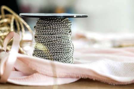 A bobbin wound with a silver chain stands on the details of clothing.