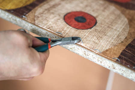 The workflow of restoration of upholstered furniture. Overworked male hands remove the old upholstery from the wooden frame of the sofa. A man, caucasian, works with flat teeth.の写真素材