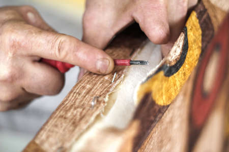 The workflow of restoration of upholstered furniture. Overworked male hands remove the old upholstery from the wooden frame of the sofa. A man, caucasian, works with flat teeth.の写真素材