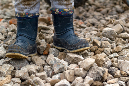 Childrens feet in dirty rubber boots on the rubble road. A walk in cloudy weather. An authentic snapshot. .の写真素材