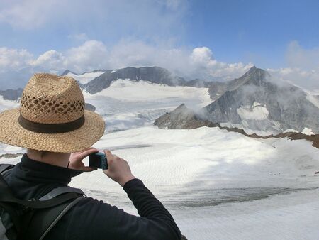Man with hat taking a photo of an alpine panorama