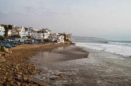 Surfer on huge wave just in front of Taghazout cityscape with fishing boats.の写真素材