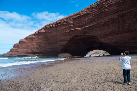 Man taking photo of Legzira rock formation - horizontal.の写真素材