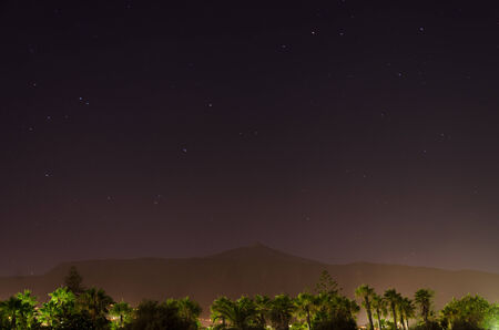 Satrs over city with palm trees in front of view and vulkano in the backgroundの写真素材