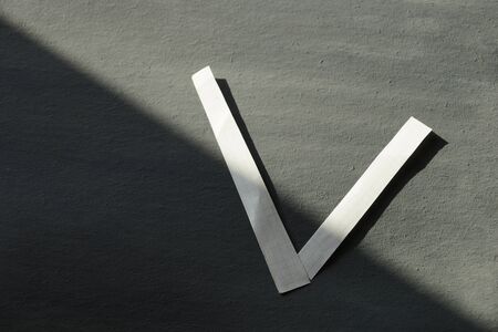 concept. election.the letter V win or tick is made of white paper on grey cardboard light and shadow.の写真素材