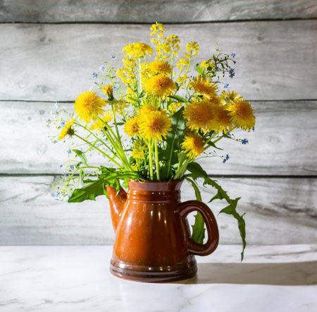 Still life with yellow dandelions in a teapot on a white marble table. The concept is a bright healthy life.の写真素材