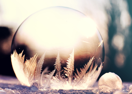 Purple frozen soap bubble ball on snow in sunset, crystal formation, winter background with copy spaceの写真素材