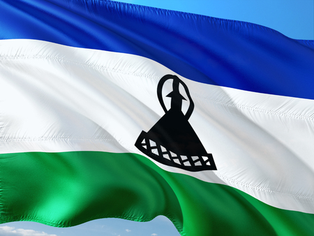 Flag of Lesotho waving in the wind against deep blue sky. High quality fabric.の写真素材
