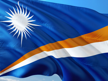 Flag of Marshall Islands waving in the wind against deep blue sky. High quality fabric.の写真素材