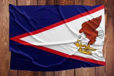 Flag of American Samoa on a wooden table background. Wrinkled Samoan flag top view.の写真素材