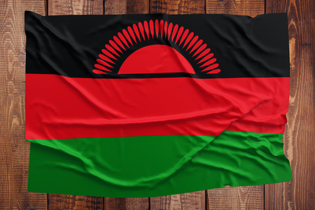 Flag of Malawi on a wooden table background. Wrinkled Malawian flag top view.の写真素材