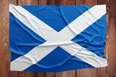 Flag of Scotland on a wooden table background. Wrinkled Scottish flag top view.の写真素材