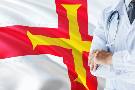 Doctor standing with stethoscope on Guernsey flag background. National healthcare system concept, medical theme.の写真素材