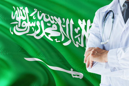 Saudi Doctor standing with stethoscope on Saudi Arabia flag background. National healthcare system concept, medical theme.の写真素材