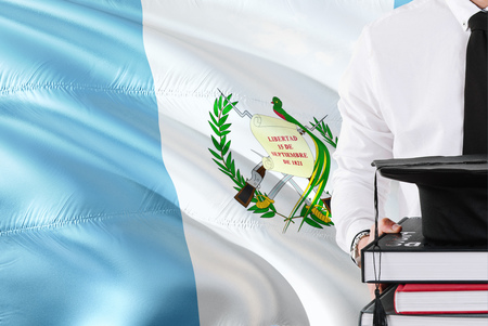 Successful Guatemalan student education concept. Holding books and graduation cap over Guatemala flag background.の写真素材
