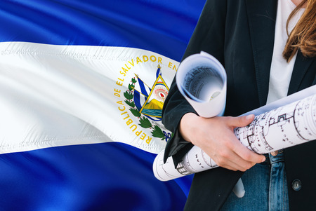 Salvadoran Architect woman holding blueprint against El Salvador waving flag background....