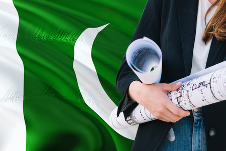 Pakistani Architect woman holding blueprint against Pakistan waving flag background. Construction and architecture concept.の写真素材