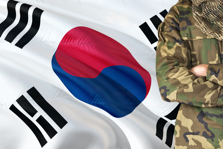 Crossed arms South Korean soldier with national waving flag on background - South Korea Military theme.の写真素材