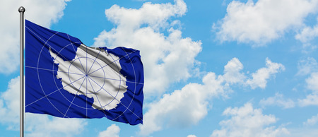 Antarctica flag waving in the wind against white cloudy blue sky. Diplomacy concept, international...