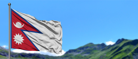 Nepal flag waving in the blue sky with green fields at mountain peak background. Nature theme.の写真素材