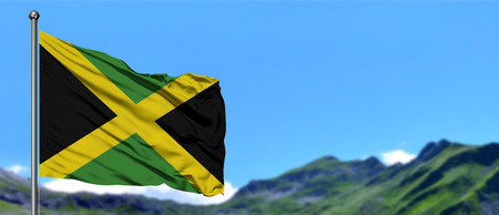 Jamaica flag waving in the blue sky with green fields at mountain peak background. Nature theme.の写真素材