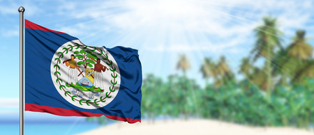 Waving Belize flag in the sunny blue sky with summer beach background. Vacation theme, holiday concept.の写真素材