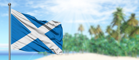 Waving Scotland flag in the sunny blue sky with summer beach background. Vacation theme, holiday concept.の写真素材