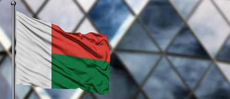 Madagascar flag waving in the wind against blurred modern building. Business concept. National cooperation theme.の写真素材