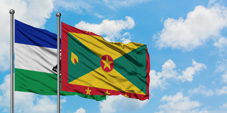 Lesotho and Grenada flag waving in the wind against white cloudy blue sky together. Diplomacy concept, international relations.の写真素材