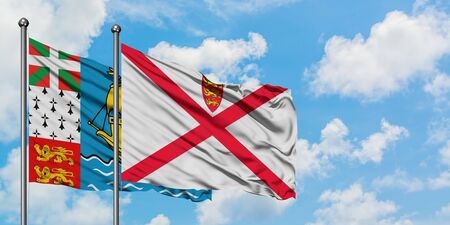 Saint Pierre And Miquelon and Jersey flag waving in the wind against white cloudy blue sky together. Diplomacy concept, international relations.の写真素材