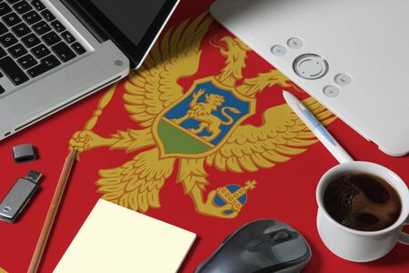 Montenegro national flag on top view work space of creative designer with laptop, computer keyboard, usb drive, graphic tablet, coffee cup, mouse on wooden table.の写真素材
