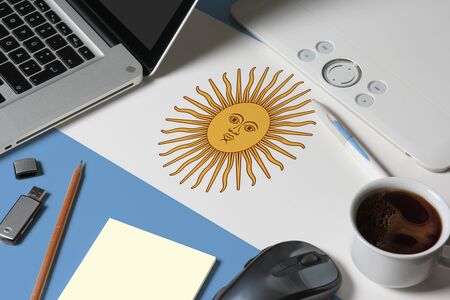 Argentina national flag on top view work space of creative designer with laptop, computer keyboard, usb drive, graphic tablet, coffee cup, mouse on wooden table.の写真素材